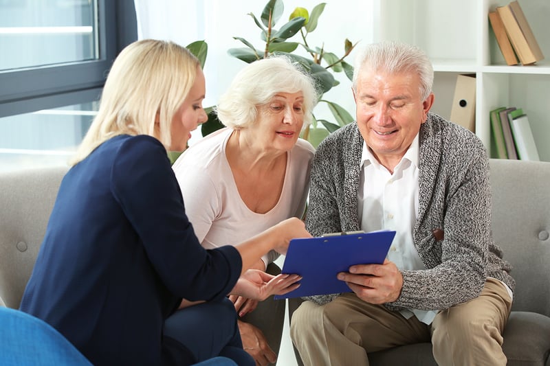 A female real estate agent sitting on a couch with a senior couple and showing them paperwork