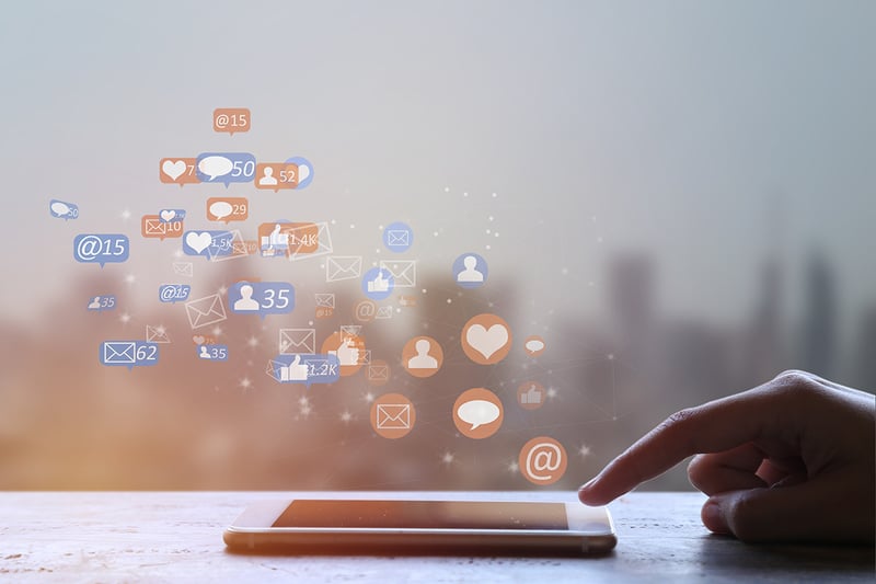 Finger touching cell phone on abstract city background with social media and communication icons floating above screen