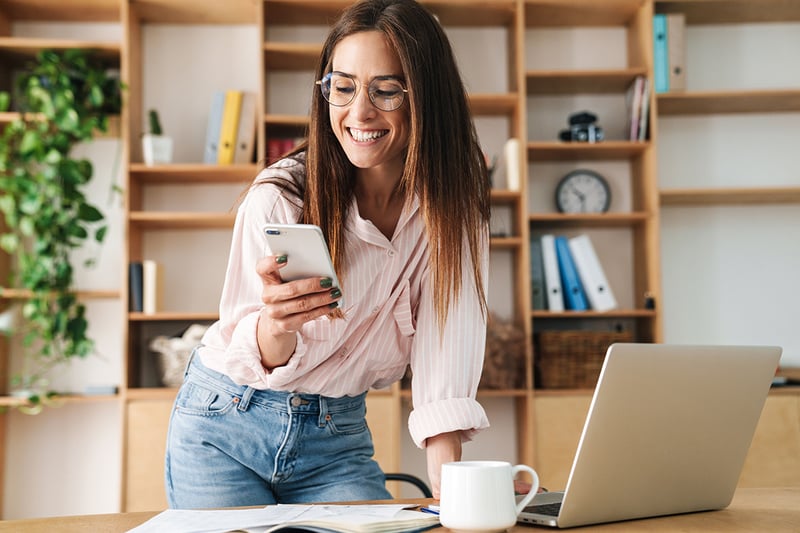Businesswoman using smartphone while working with laptop