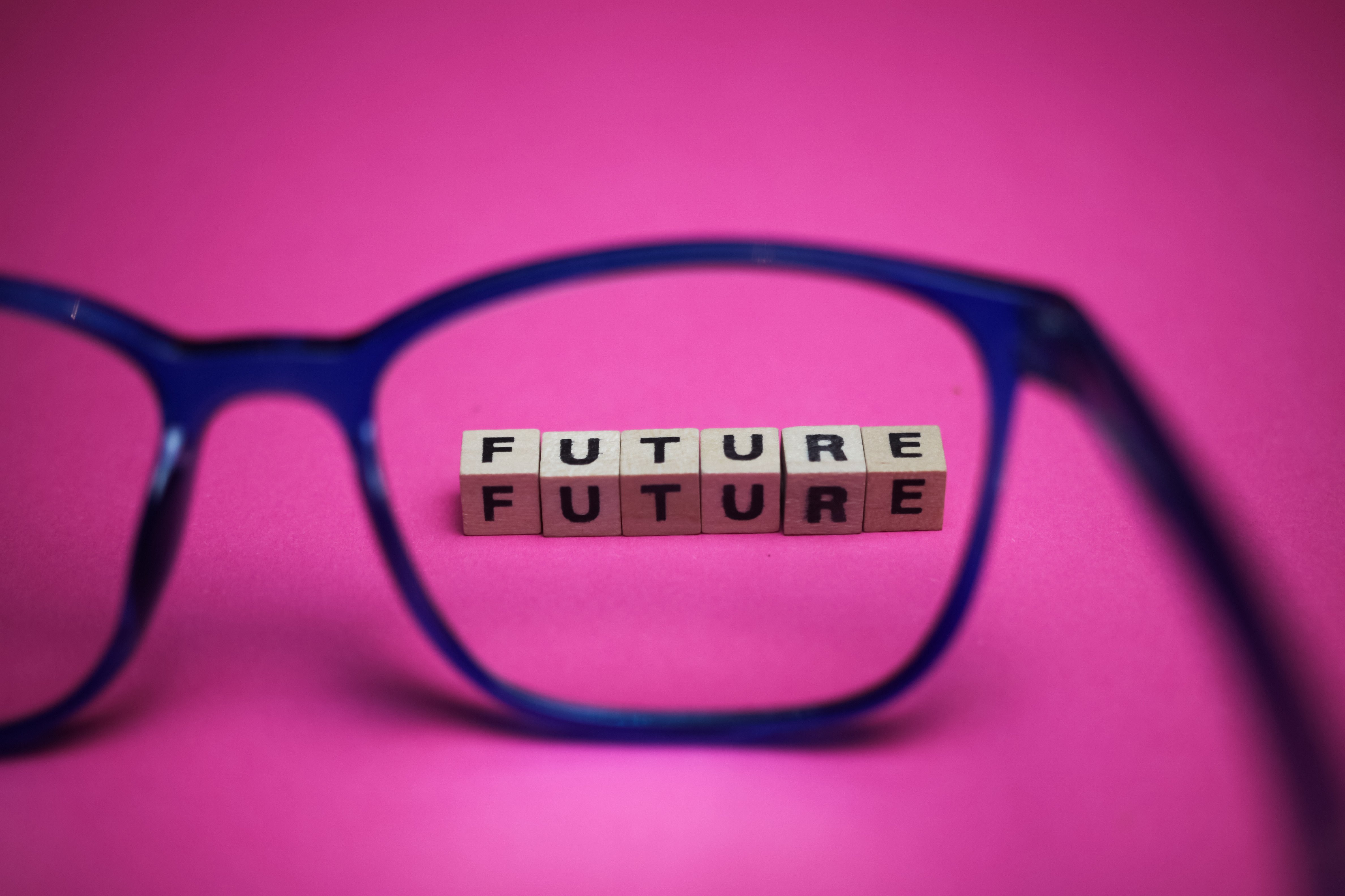 View through isolated blue eyeglasses on word future with pink background (focus on upper row of text)